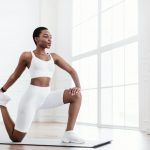 Feliz joven mujer negra estirando la pierna haciendo ejercicio en la estera de yoga