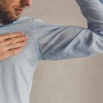 Hombre con hiperhidrosis sudando mucho bajo la axila con camisa azul, gris.