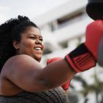 Mujer con curvas y entrenadora personal haciendo sesiones de entrenamiento de boxeo al aire libre - Enfoque en la cara