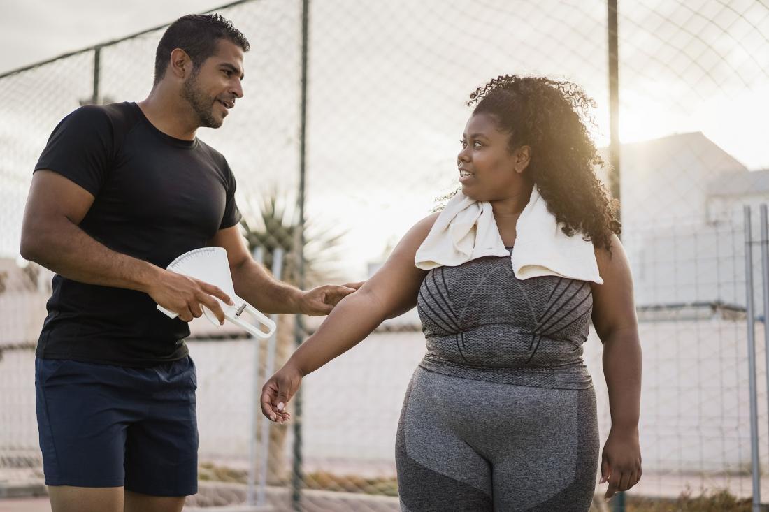 Mujer con curvas con su entrenador personal midiendo la grasa corporal al aire libre