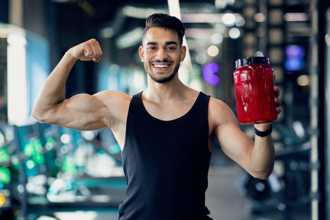Fitness Supplements. Musculate Arab Man Holding Container With Protein Powder In Gym Suplementos de fitness. Hombre árabe musculoso sosteniendo un contenedor con proteína en polvo en el gimnasio