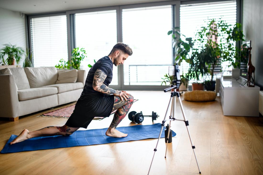 Man trainer doing online workout exercise indoors at home, using camera