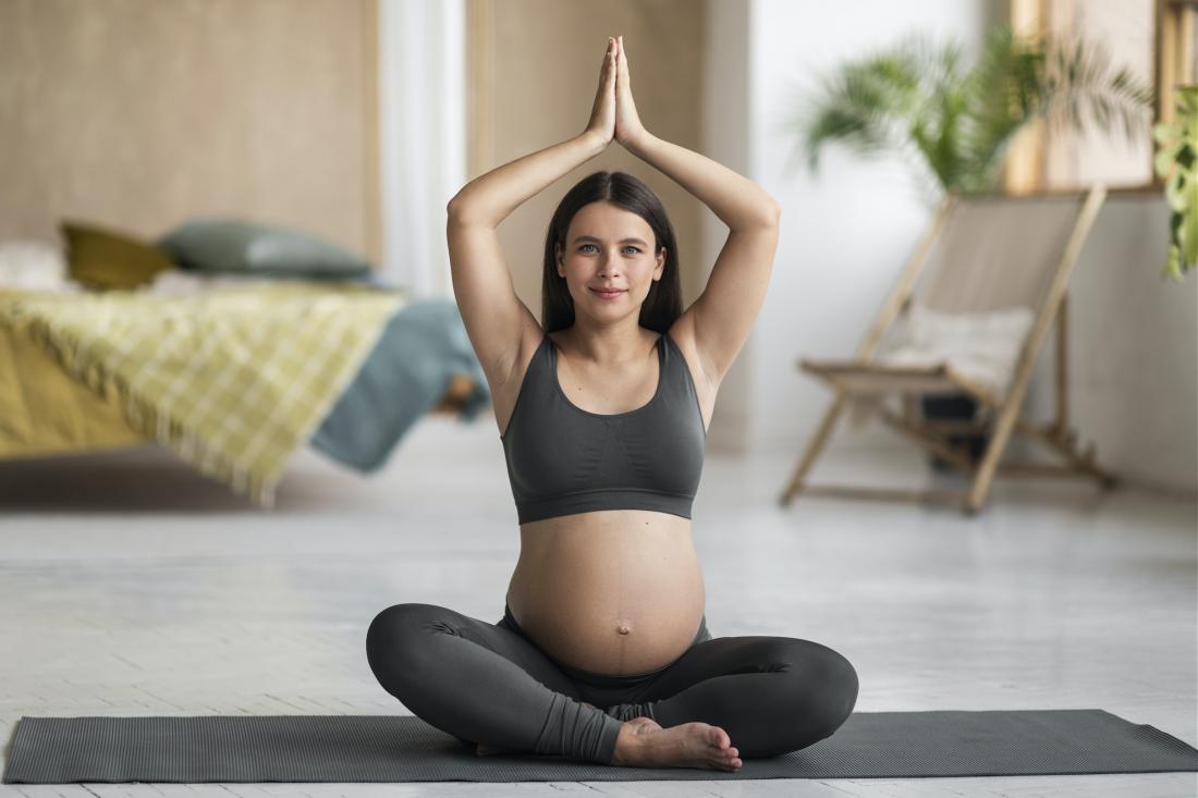 Pregnancy Yoga. Young Pregnant Woman Meditating With Hands Clasped Above Head