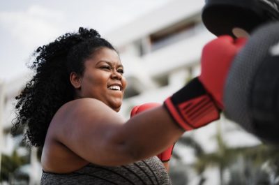 Mujer con curvas y entrenadora personal haciendo sesiones de entrenamiento de boxeo al aire libre - Enfoque en la cara