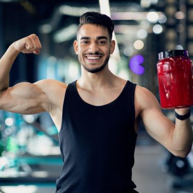 Suplementos de fitness. Hombre árabe musculoso sosteniendo un contenedor con proteína en polvo en el gimnasio
