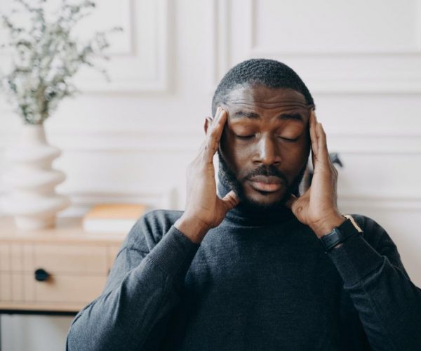 Un joven empleado africano estresado con una expresión facial frustrada que sufre de dolor de cabeza
